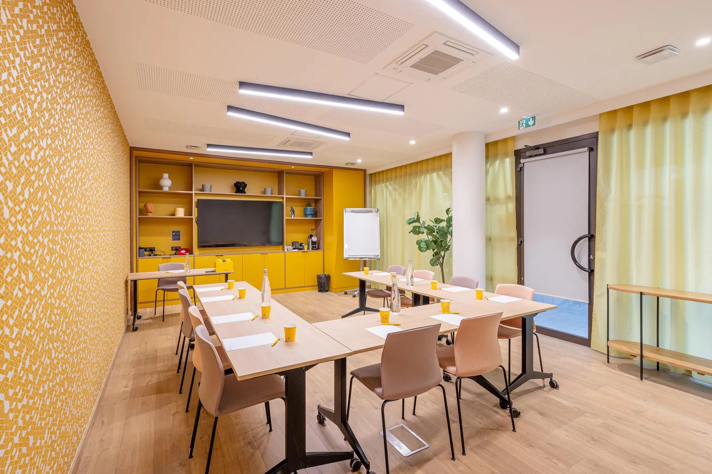 Salle de réunion avec tables, chaises, écran, projecteur et décoration murale jaune