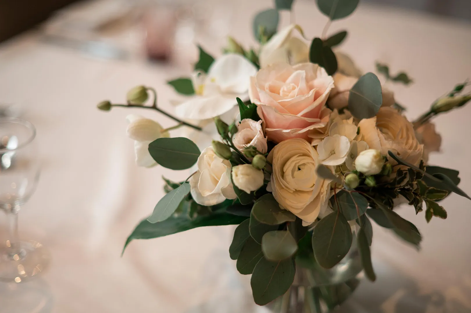 Bouquet de roses blanches et roses accompagné de feuillage vert sur une table blanche avec un verre à vin en arrière-plan