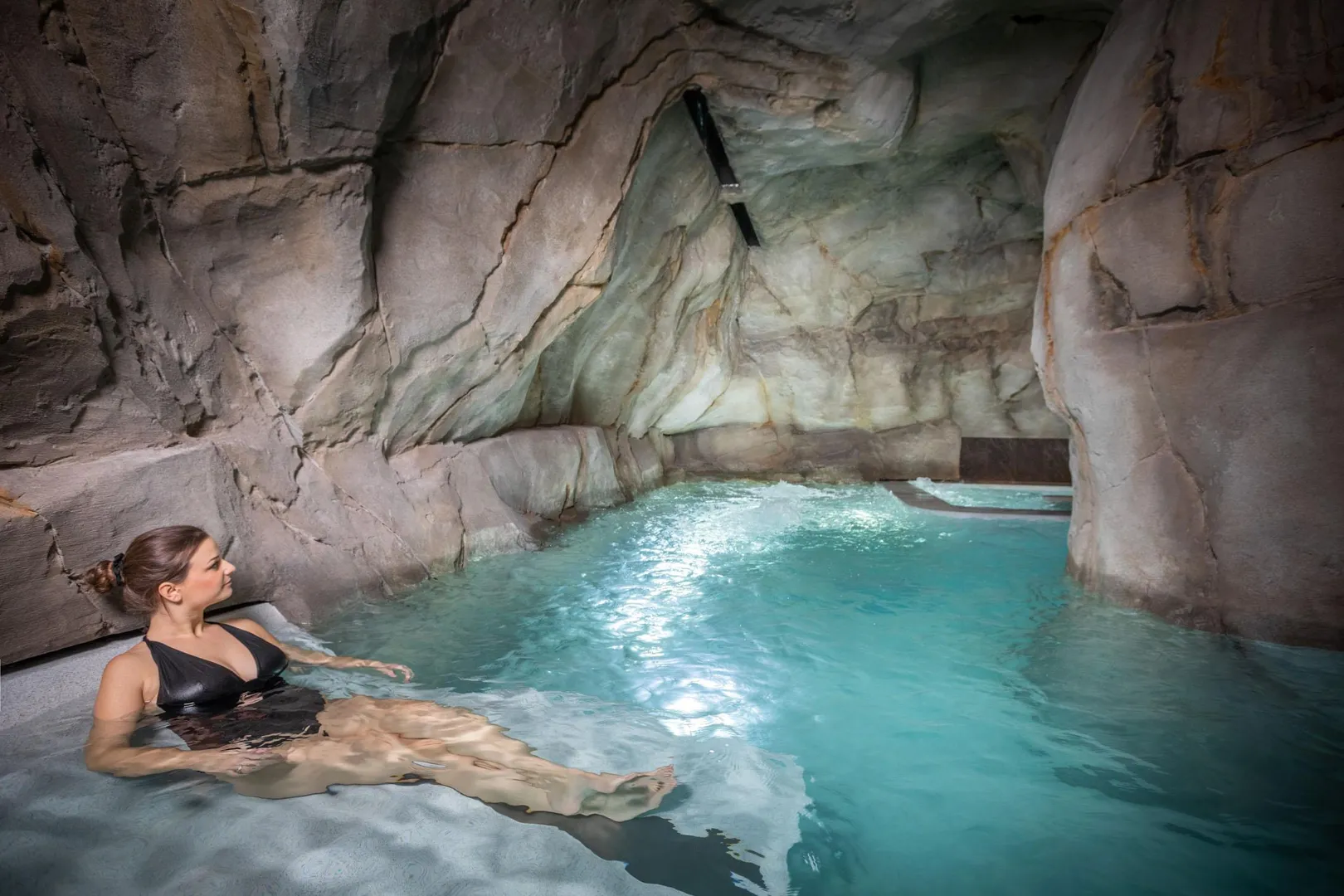 Une personne est allongée dans une piscine d'eau bleue située dans une grotte artificielle en pierre