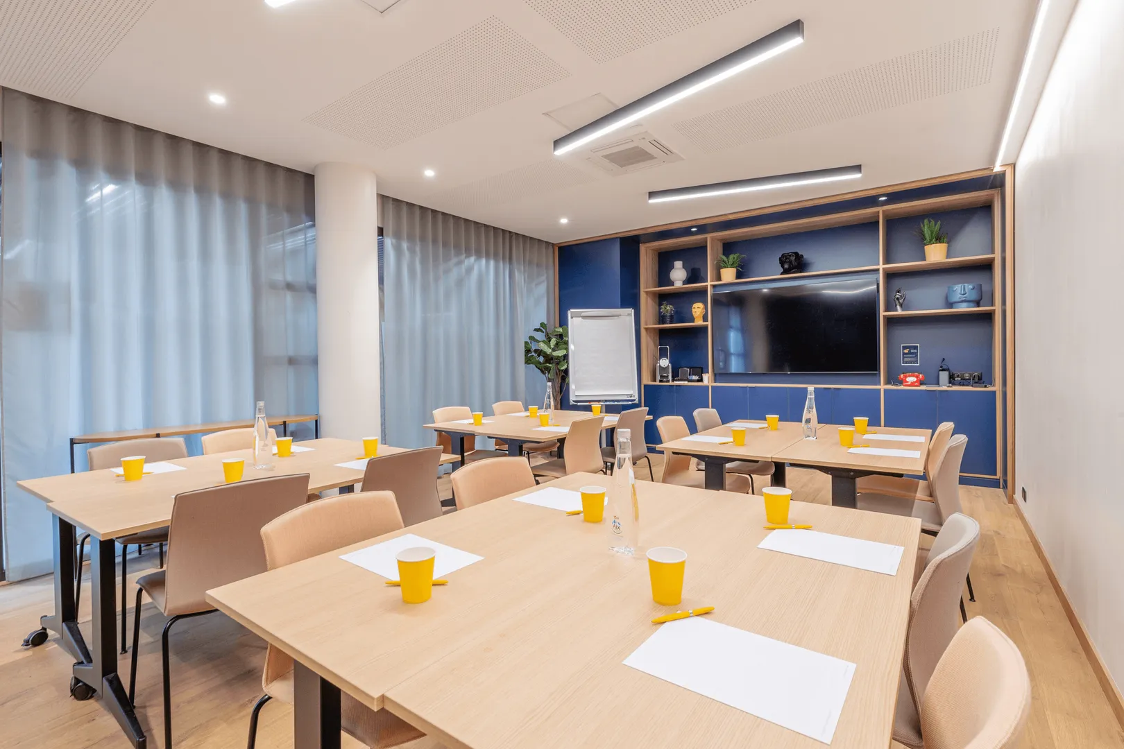 Salle de réunion avec tables, chaises, gobelets, bouteilles d'eau et un écran à l'arrière-plan