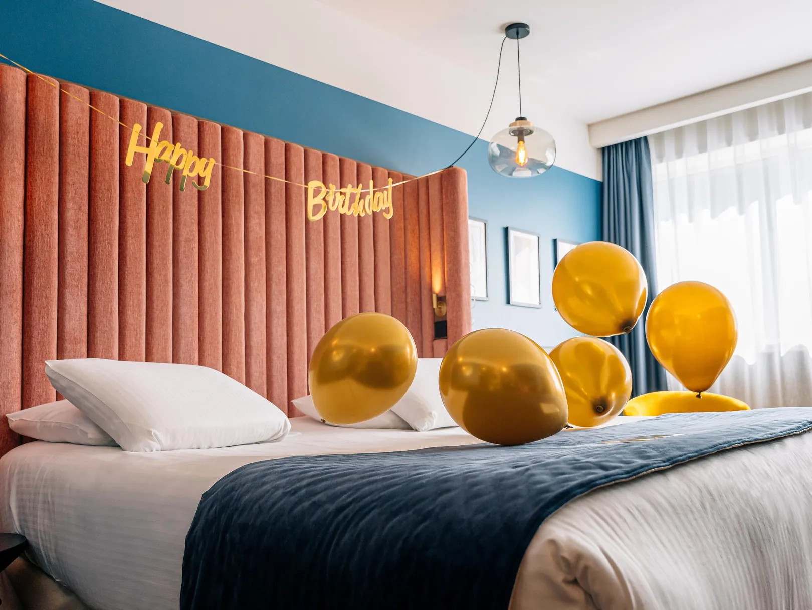 Lit avec des ballons dorés et une bannière "Happy Birthday" au-dessus de la tête de lit rouge