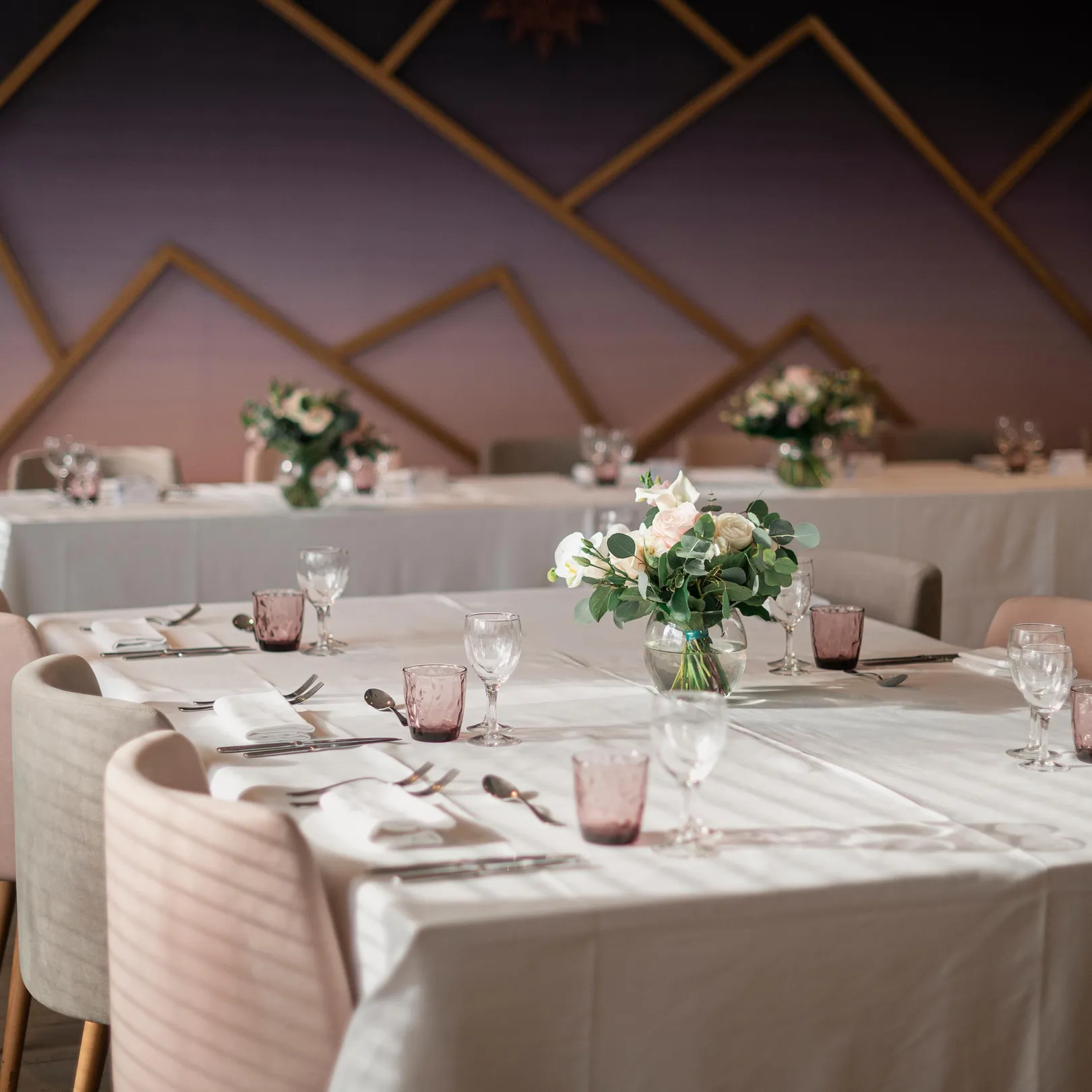 Table dressée avec des verres, des couverts et des fleurs dans un espace intérieur avec des murs décorés de motifs géométriques