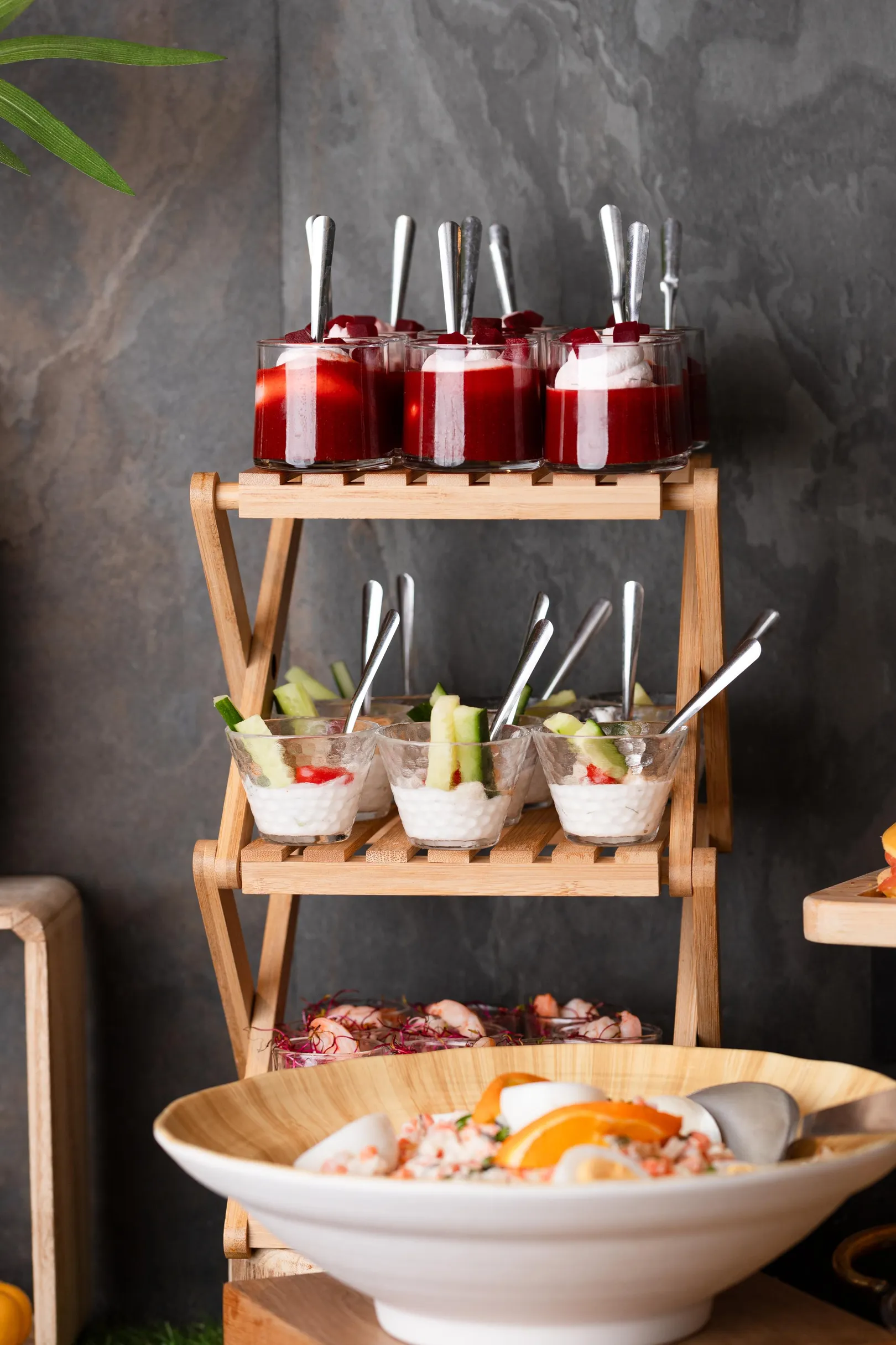 Un présentoir en bois à trois étages avec des coupes de fruits et de crème, accompagné d'une grande coupe de fruits en bas