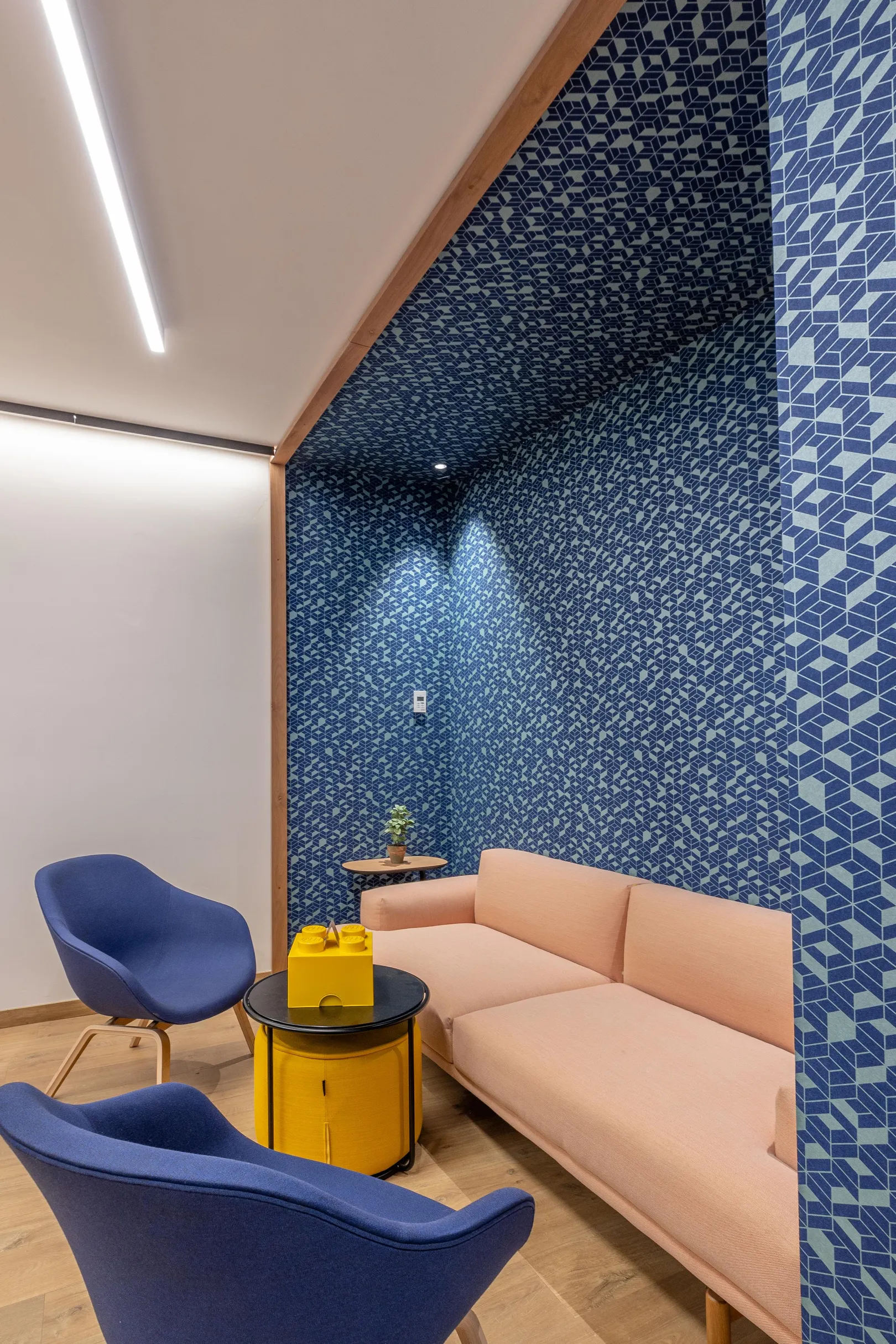 Un salon avec un canapé beige, deux fauteuils bleus et une table basse jaune, devant un mur décoré de motifs géométriques bleus et gris