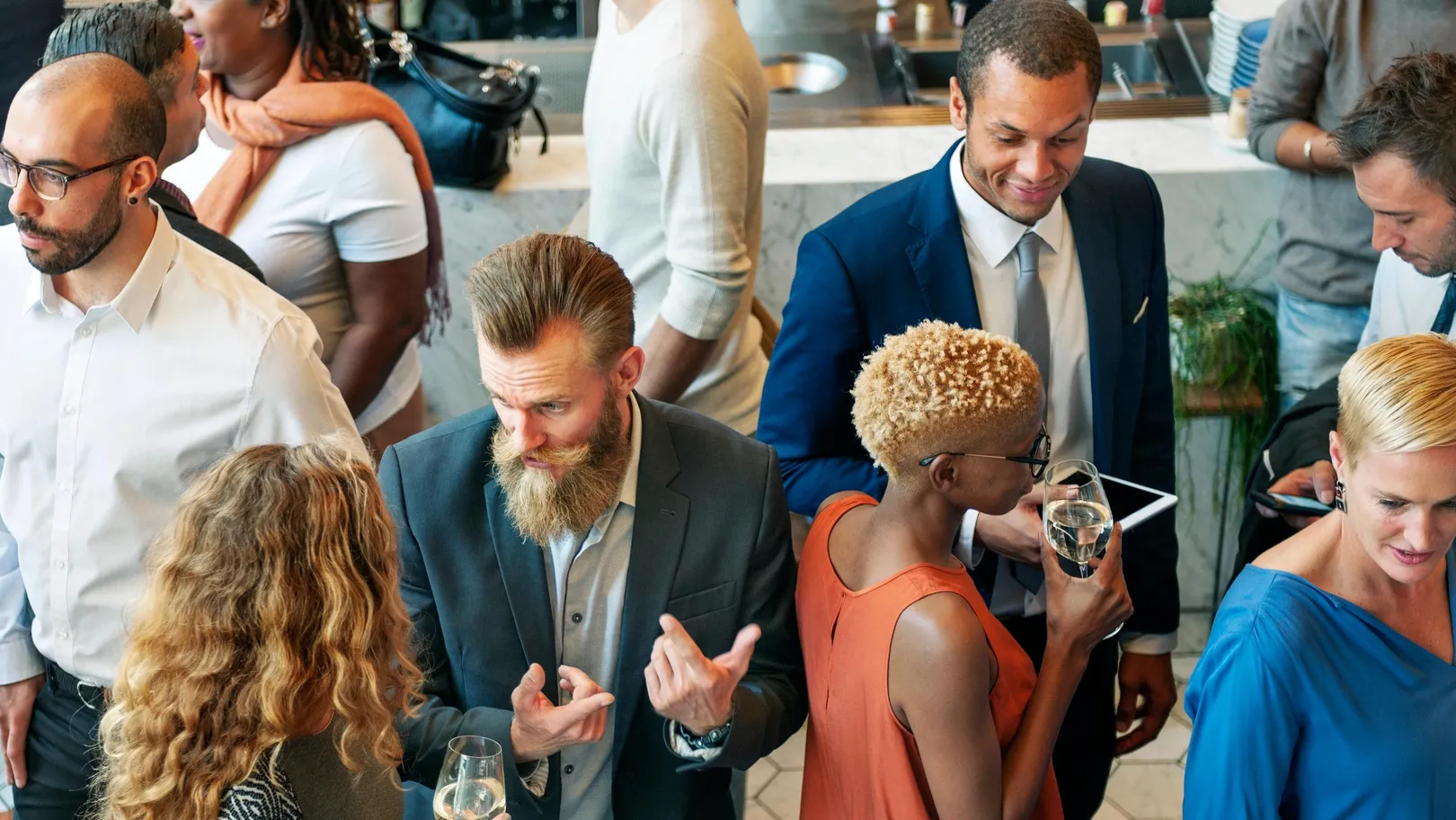 Un groupe de personnes en tenue professionnelle discute et boit des verres dans un cadre intérieur.