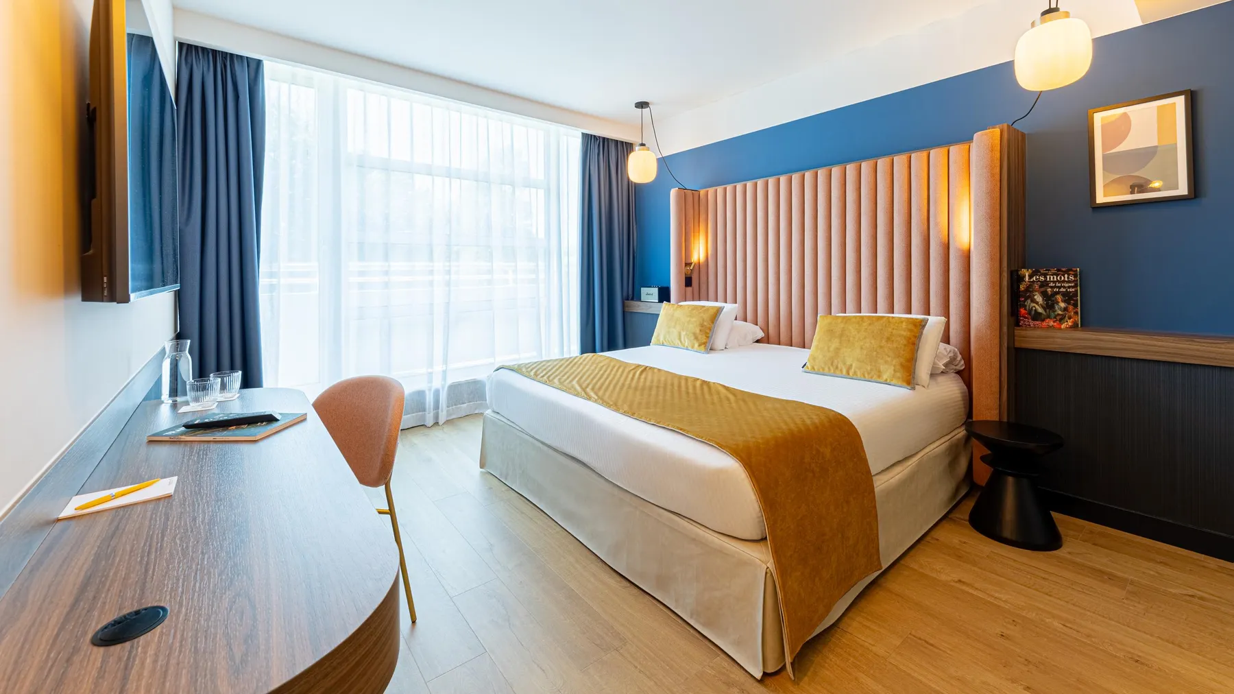 Chambre d'hôtel avec un lit double, une table de travail, des fenêtres avec des rideaux et des lumières murales