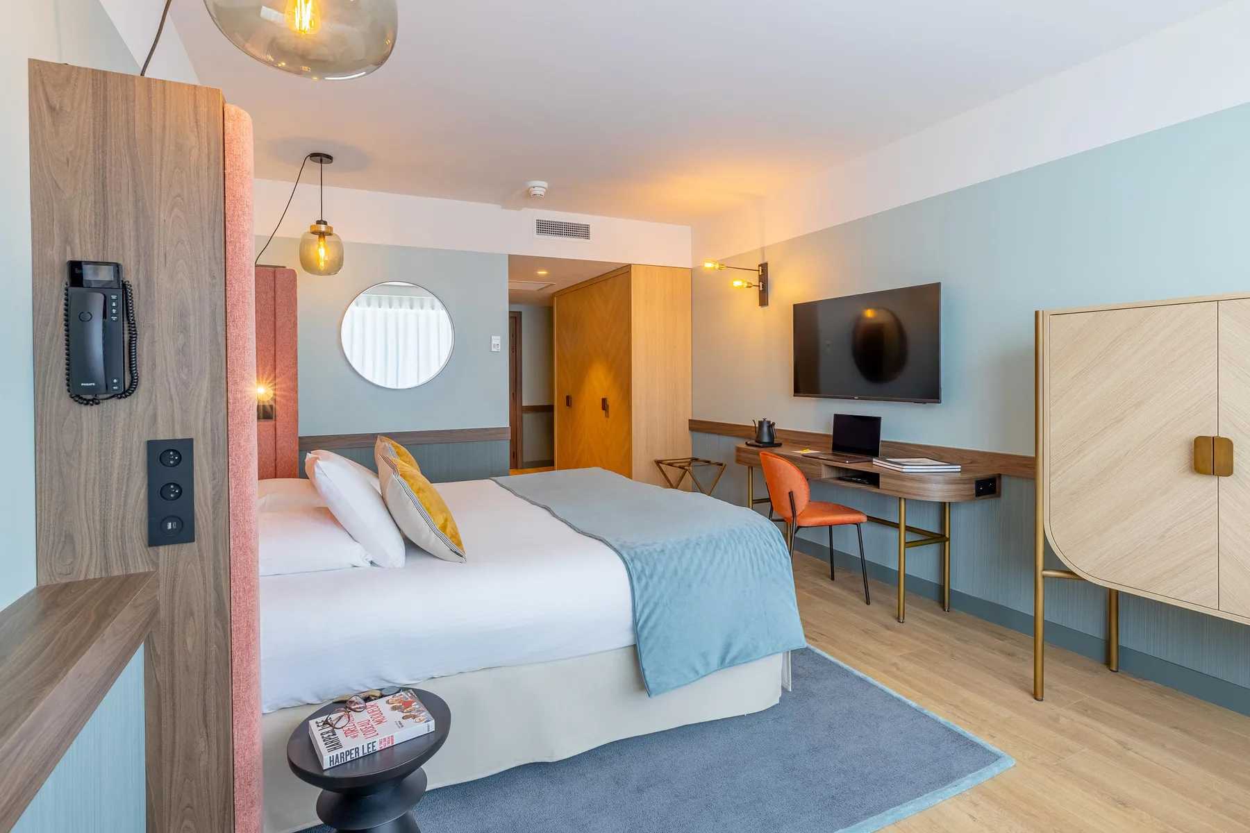 Chambre d'hôtel moderne avec lit, bureau, télévision, et éléments en bois et métal