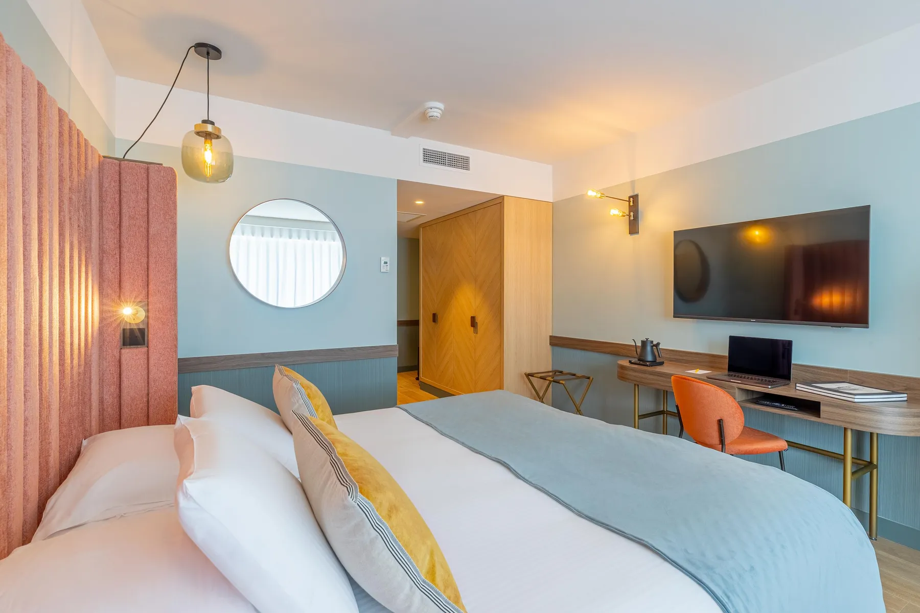 Chambre d'hôtel avec un lit double, une télévision, un bureau et des lumières murales