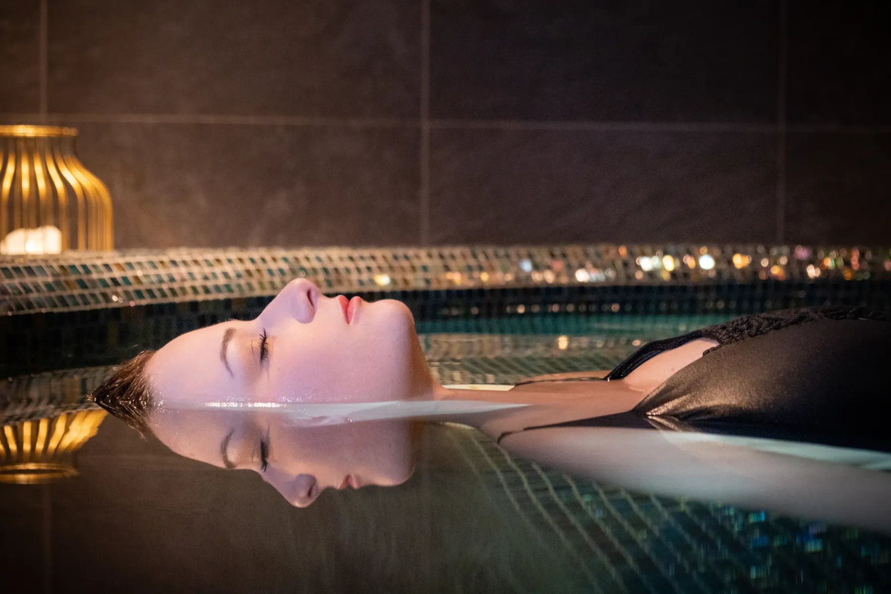 Une personne allongée sur le dos dans une piscine avec une vue nocturne floue en arrière-plan