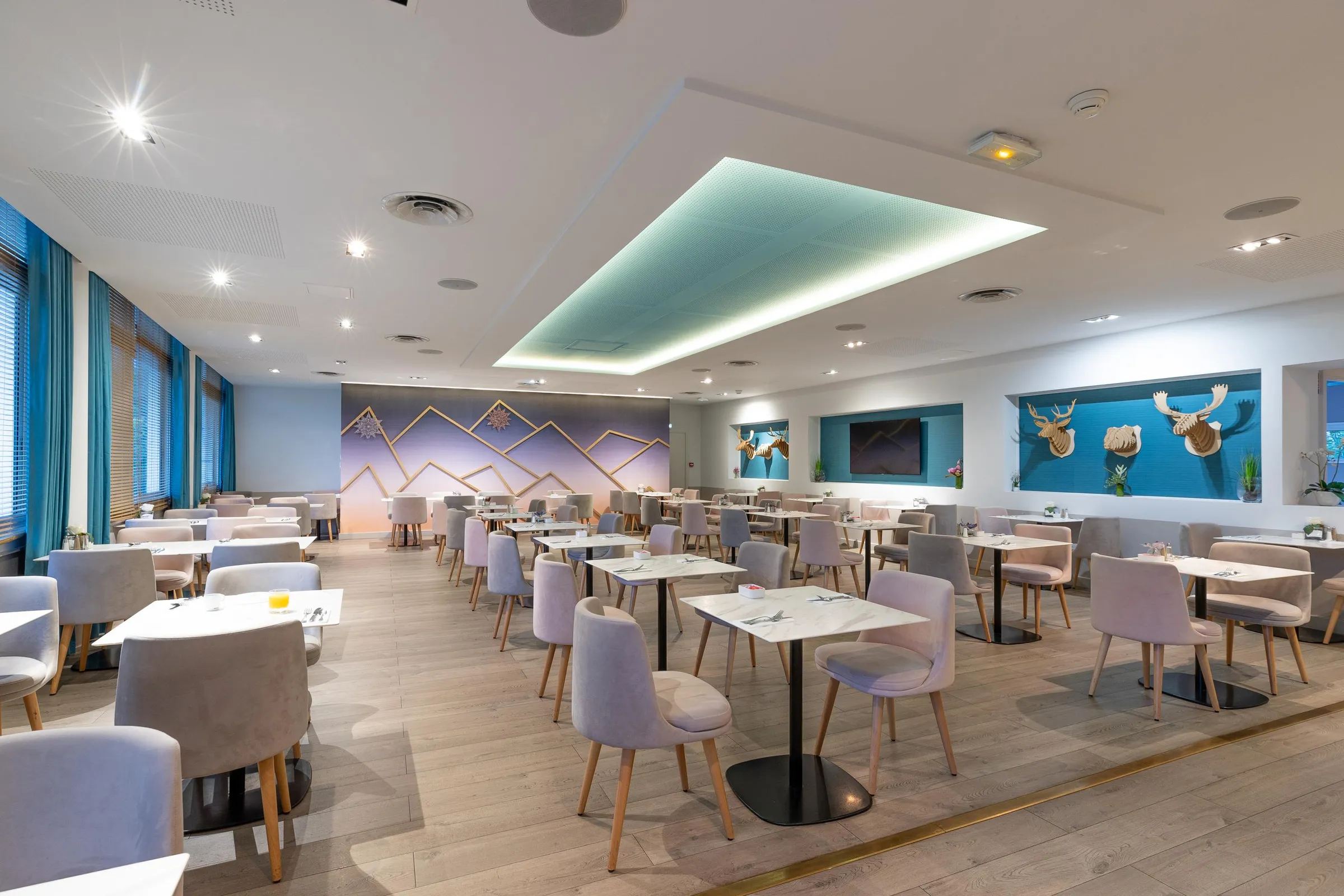 Salle de restaurant moderne avec tables rondes, chaises grises et décor mural aux motifs géométriques et animaux