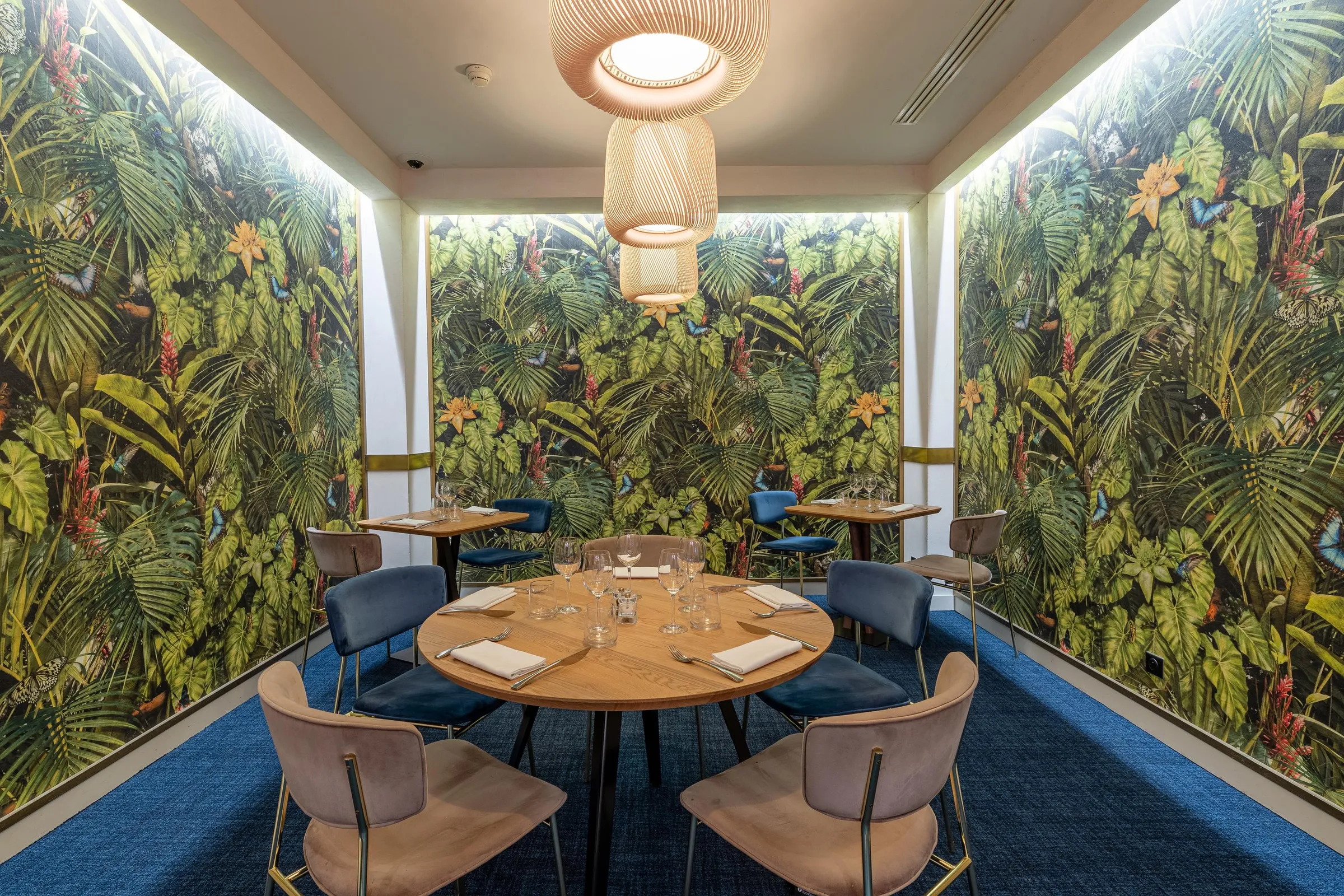 Salle à manger avec des murs couverts d'une végétation luxuriante et des tables rondes entourées de chaises rembourrées
