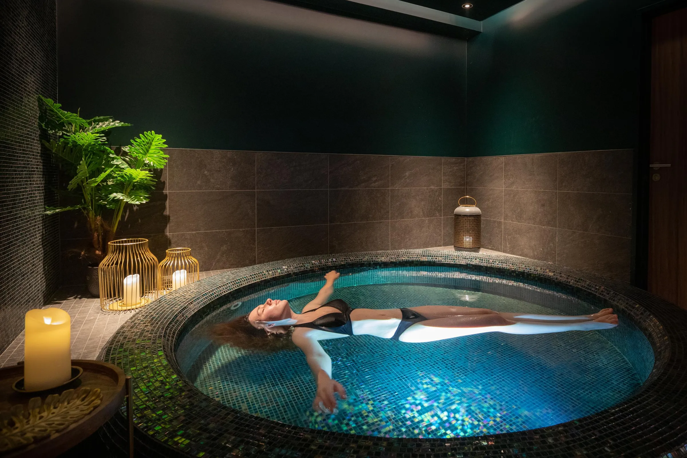 Une personne allongée dans un bain à remous circulaire entouré de bougies et de plantes vertes