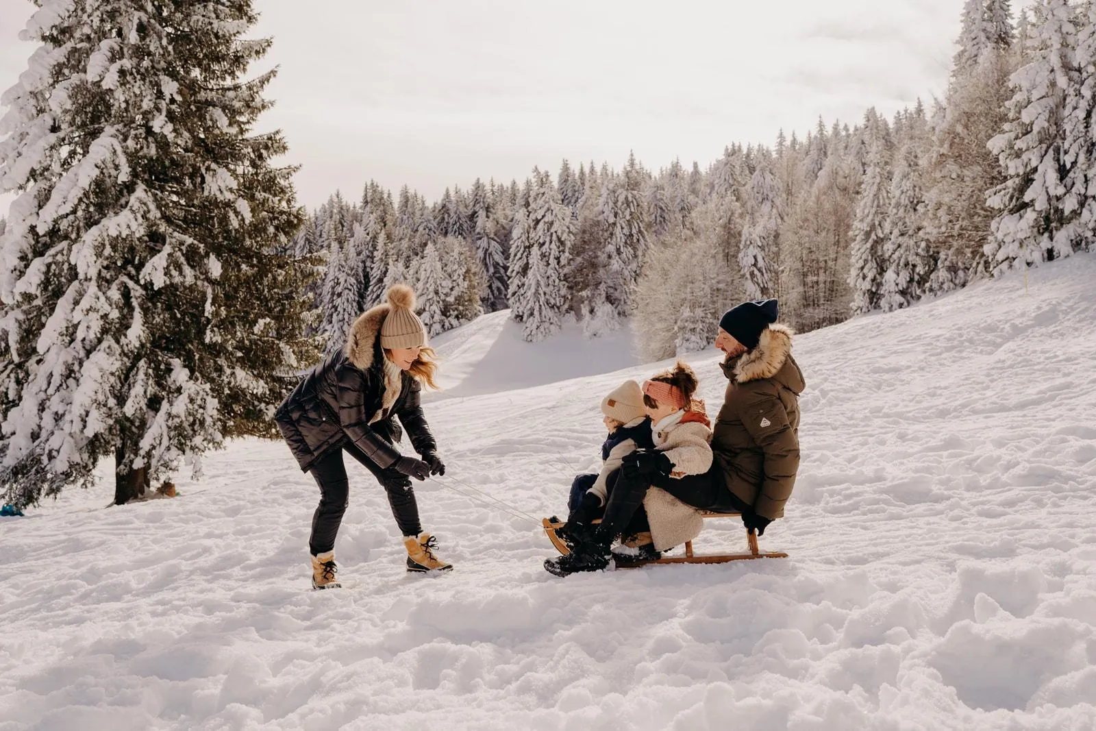 Une famille fait de la luge dans un paysage enneigé entouré d'arbres couverts de neige