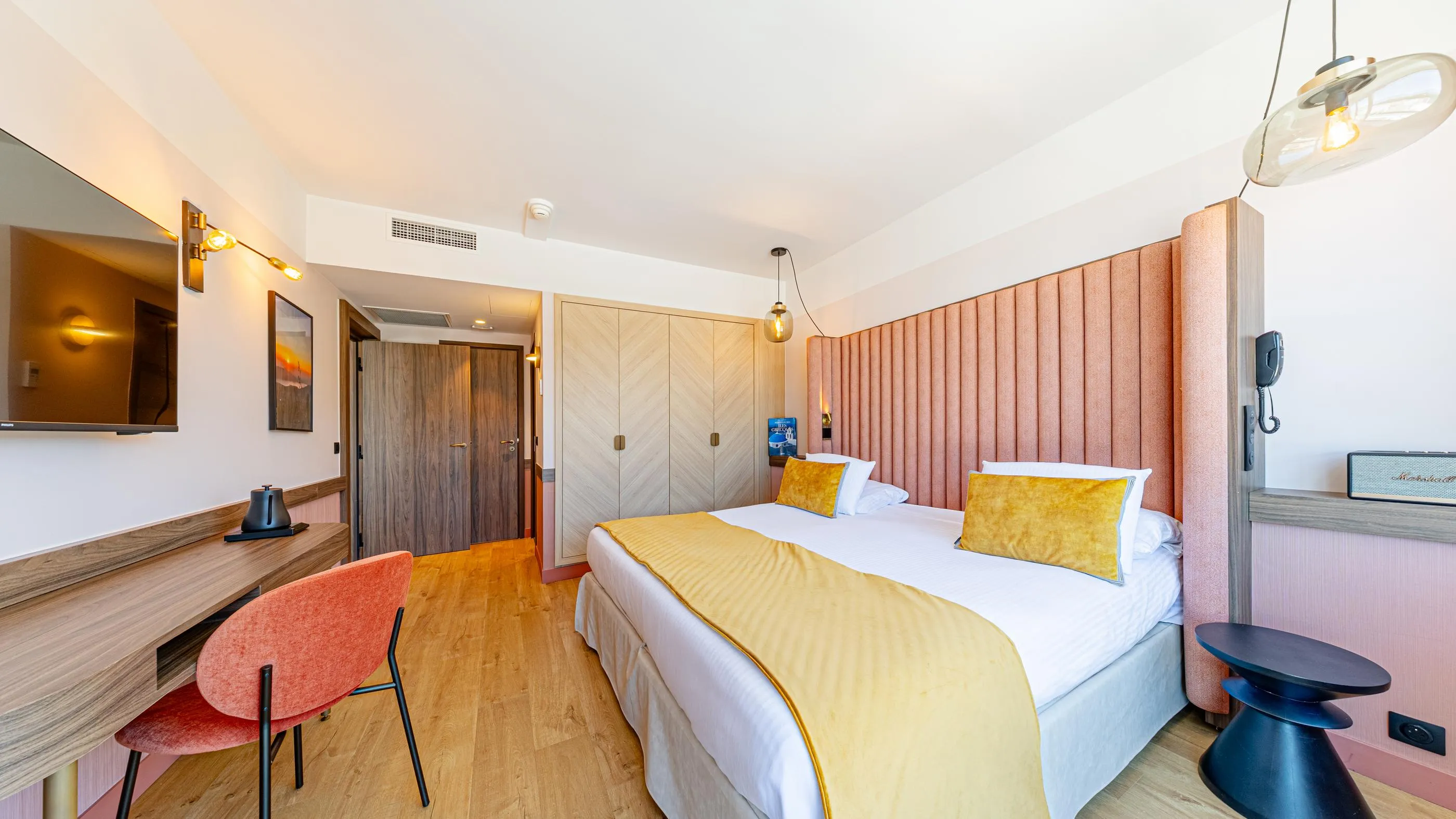 Chambre d'hôtel avec un lit double, une table de travail, une chaise et une porte ouverte sur un couloir