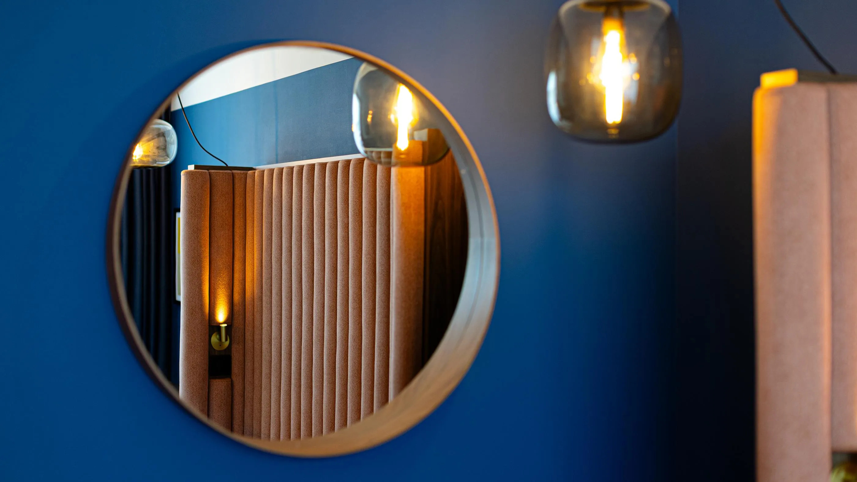 Un miroir rond reflète une pièce avec des lumières et des rideaux verticaux
