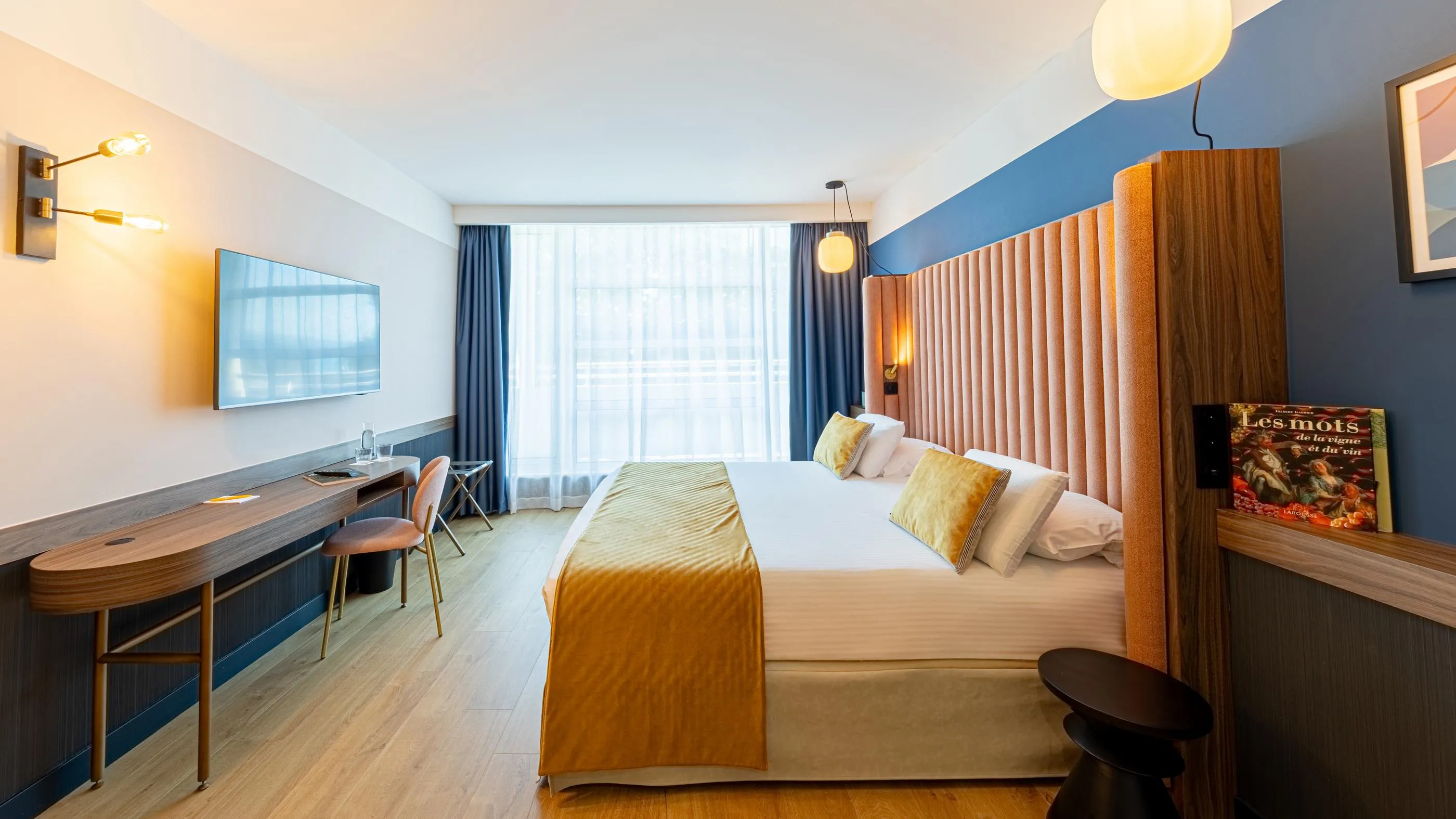 Chambre d'hôtel moderne avec un lit double, un bureau, une télévision, des fenêtres avec des rideaux et une décoration sobre et élégante