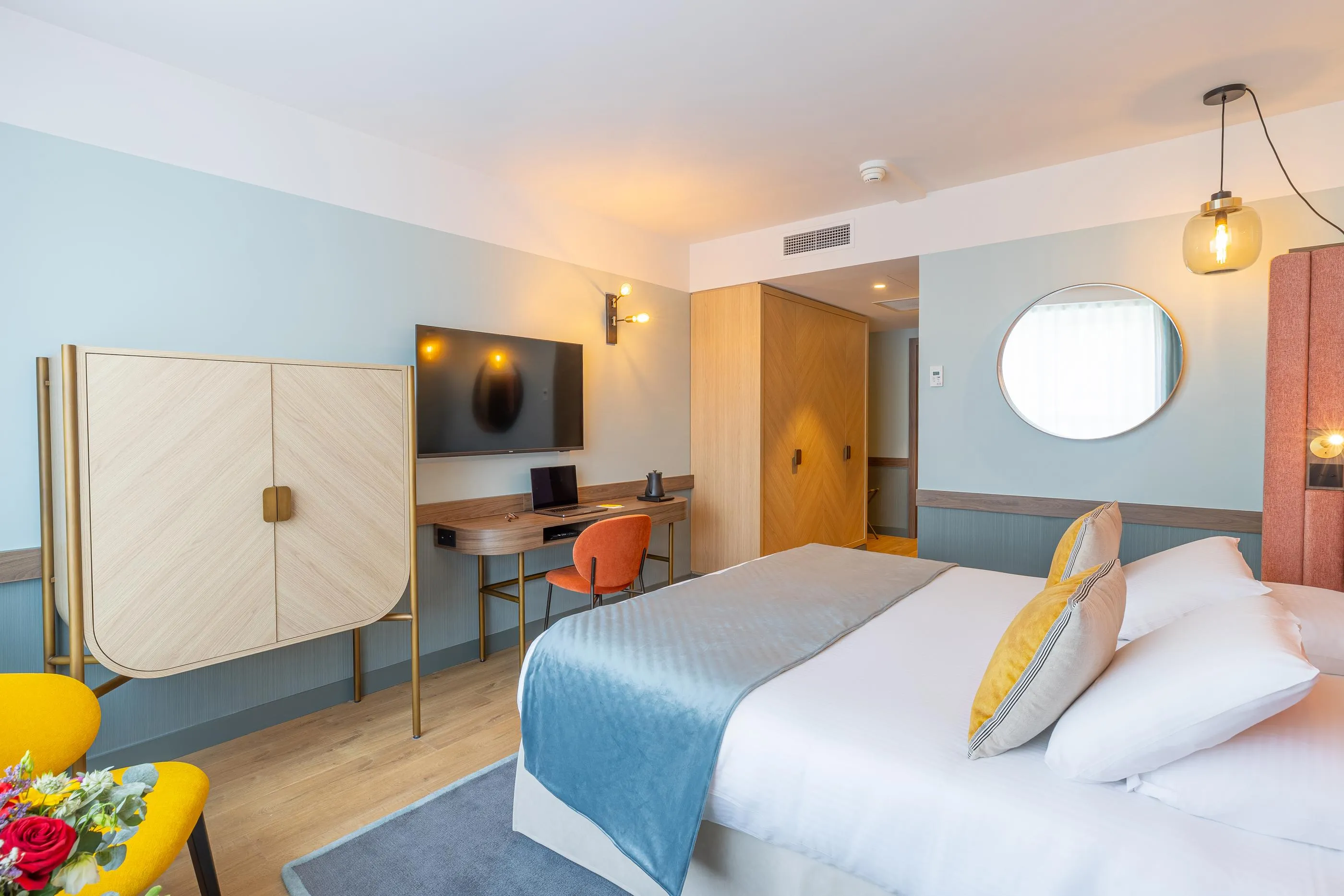 Chambre avec un lit double, un bureau, une télévision, un paravent et une chaise orange