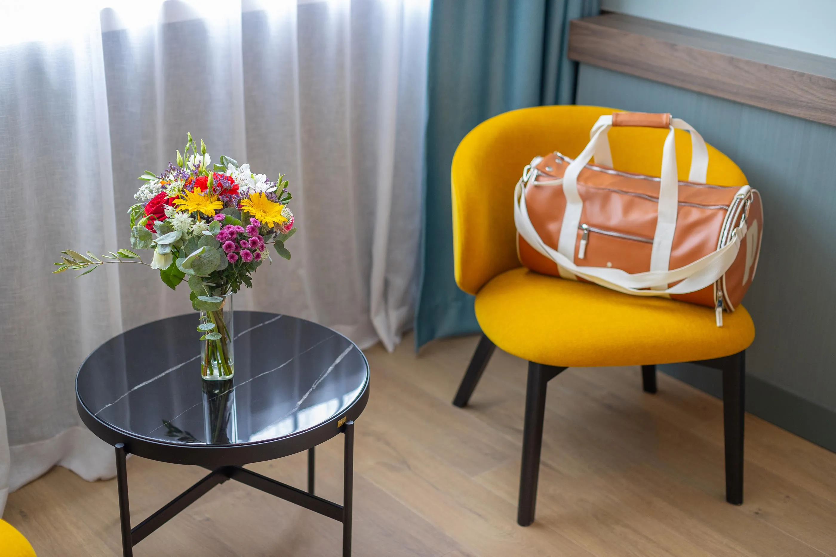 Une table ronde noire avec un vase de fleurs colorées à côté d'une chaise jaune avec un sac en cuir posé dessus