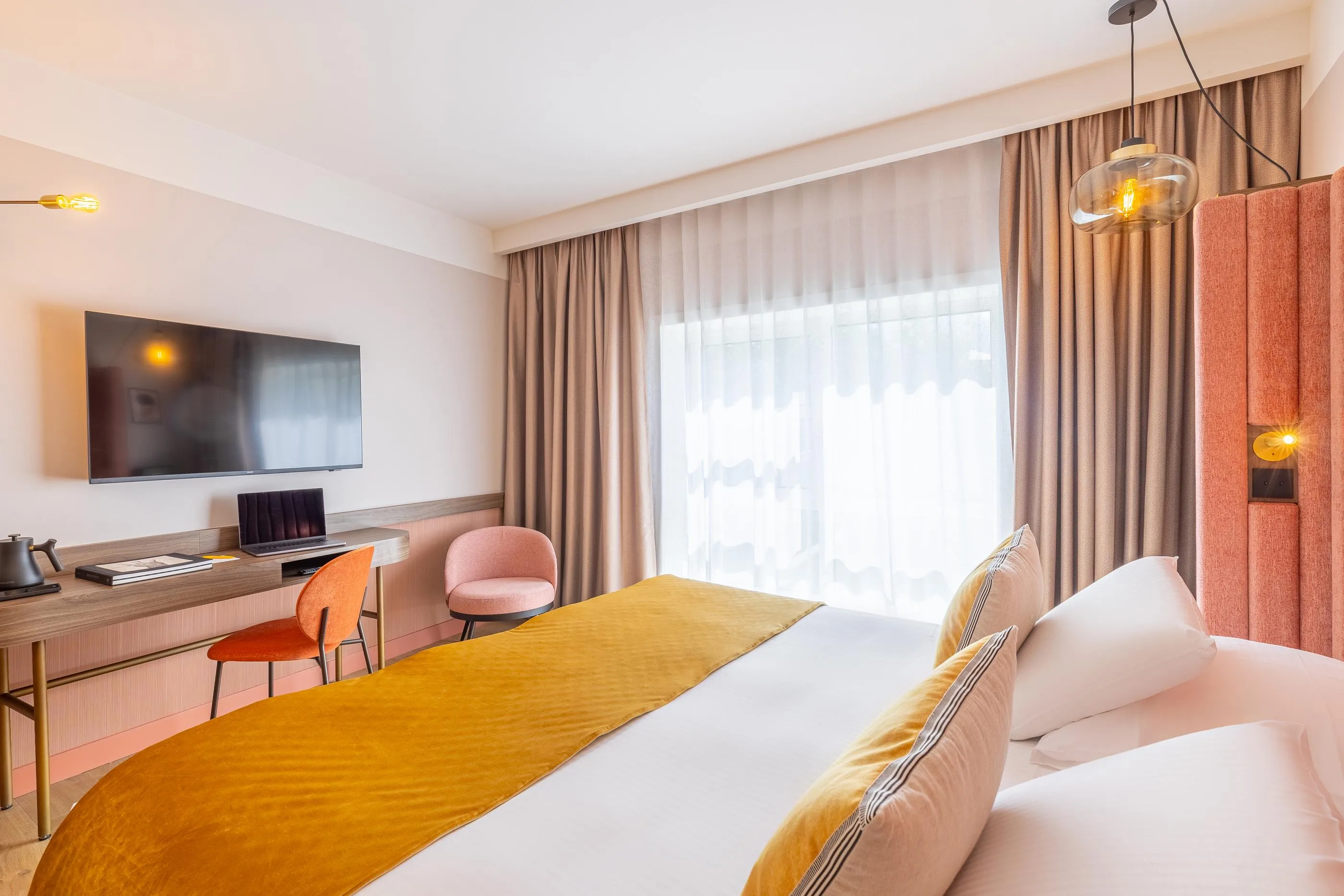 Chambre d'hôtel avec un lit double, une table de travail, un téléviseur mural et une grande fenêtre avec des rideaux