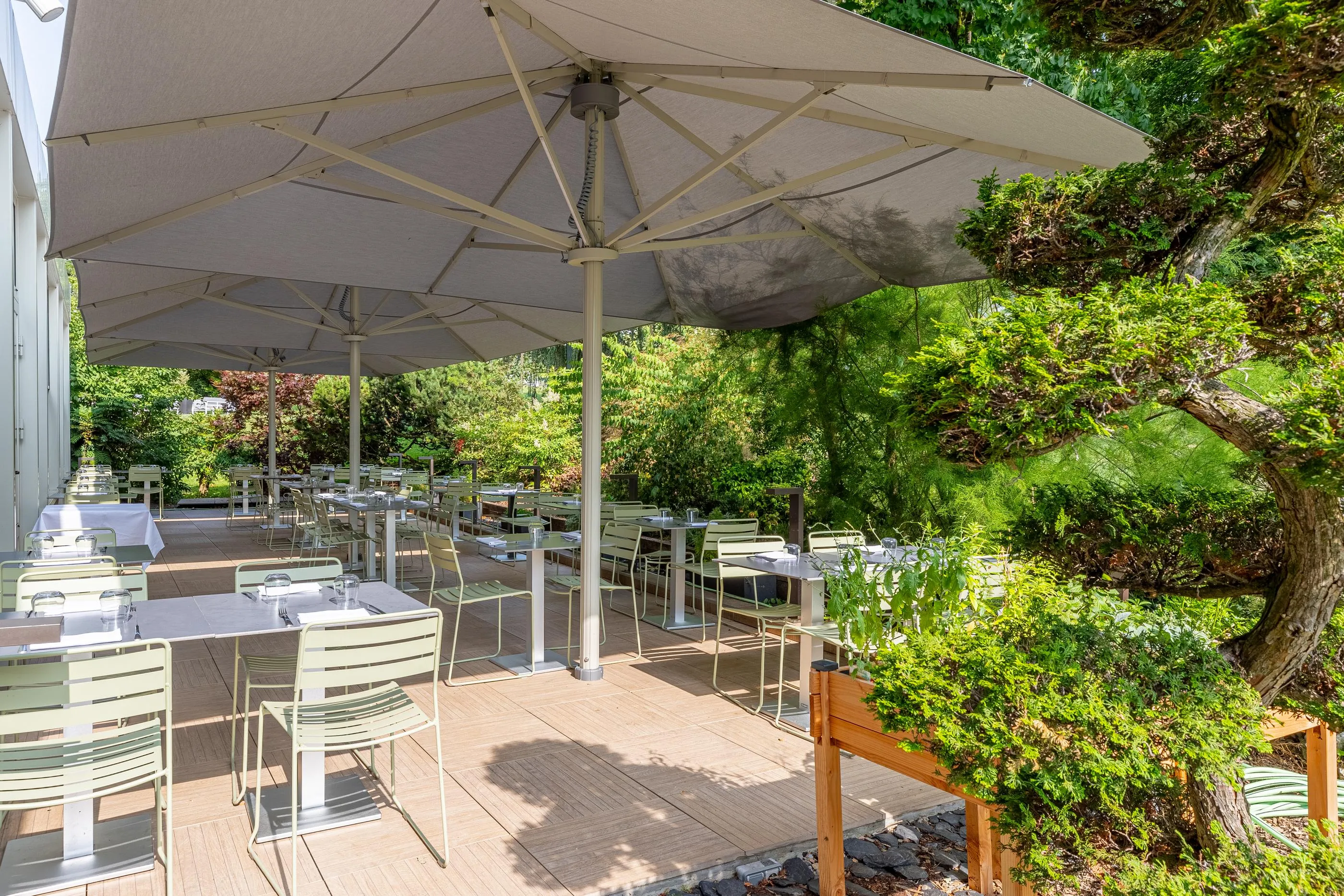 Terrasse de restaurant extérieure avec tables et chaises sous un grand parasol, entourée de verdure
