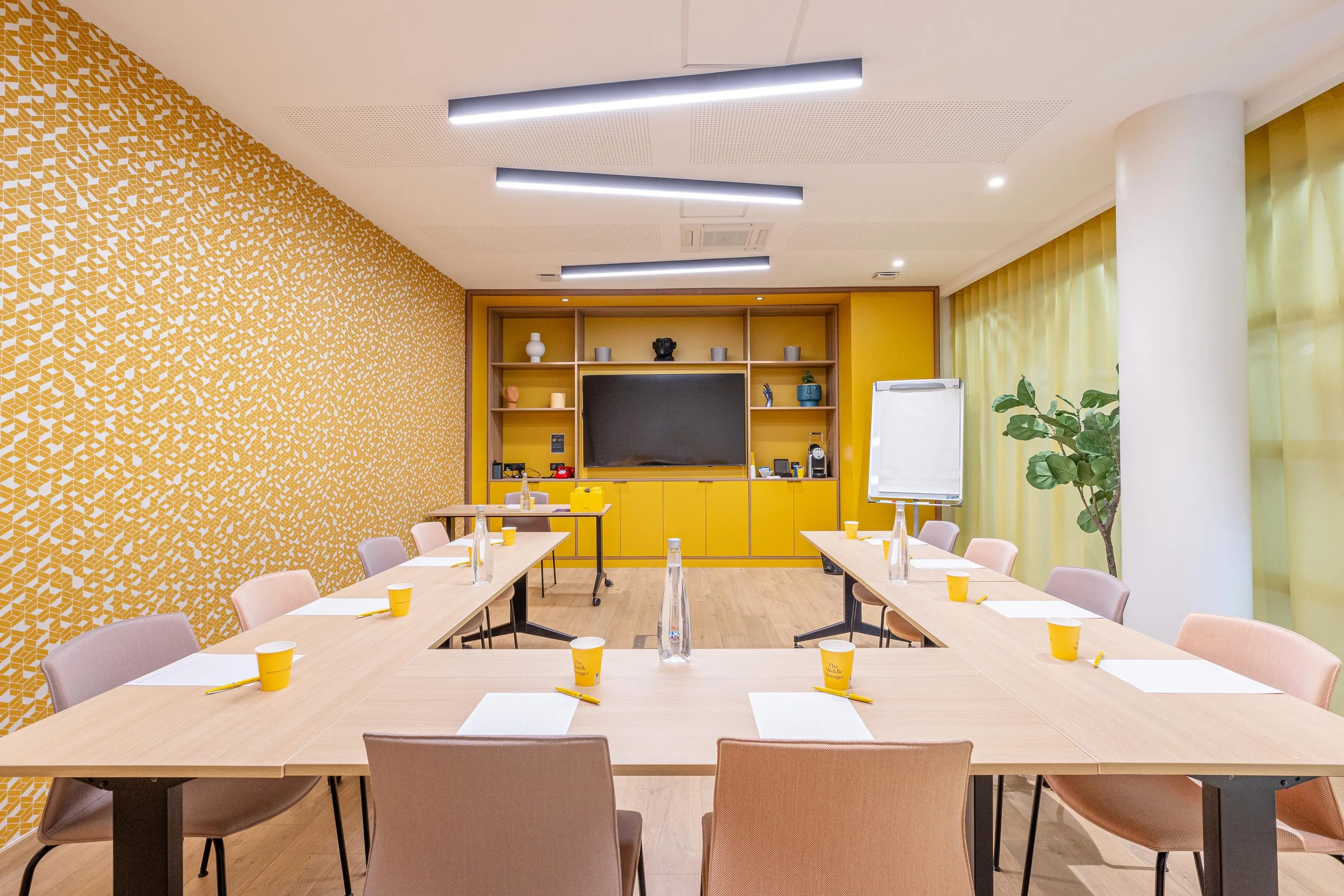 Salle de réunion avec tables, chaises, écran, tableau blanc, décoration murale et plantes