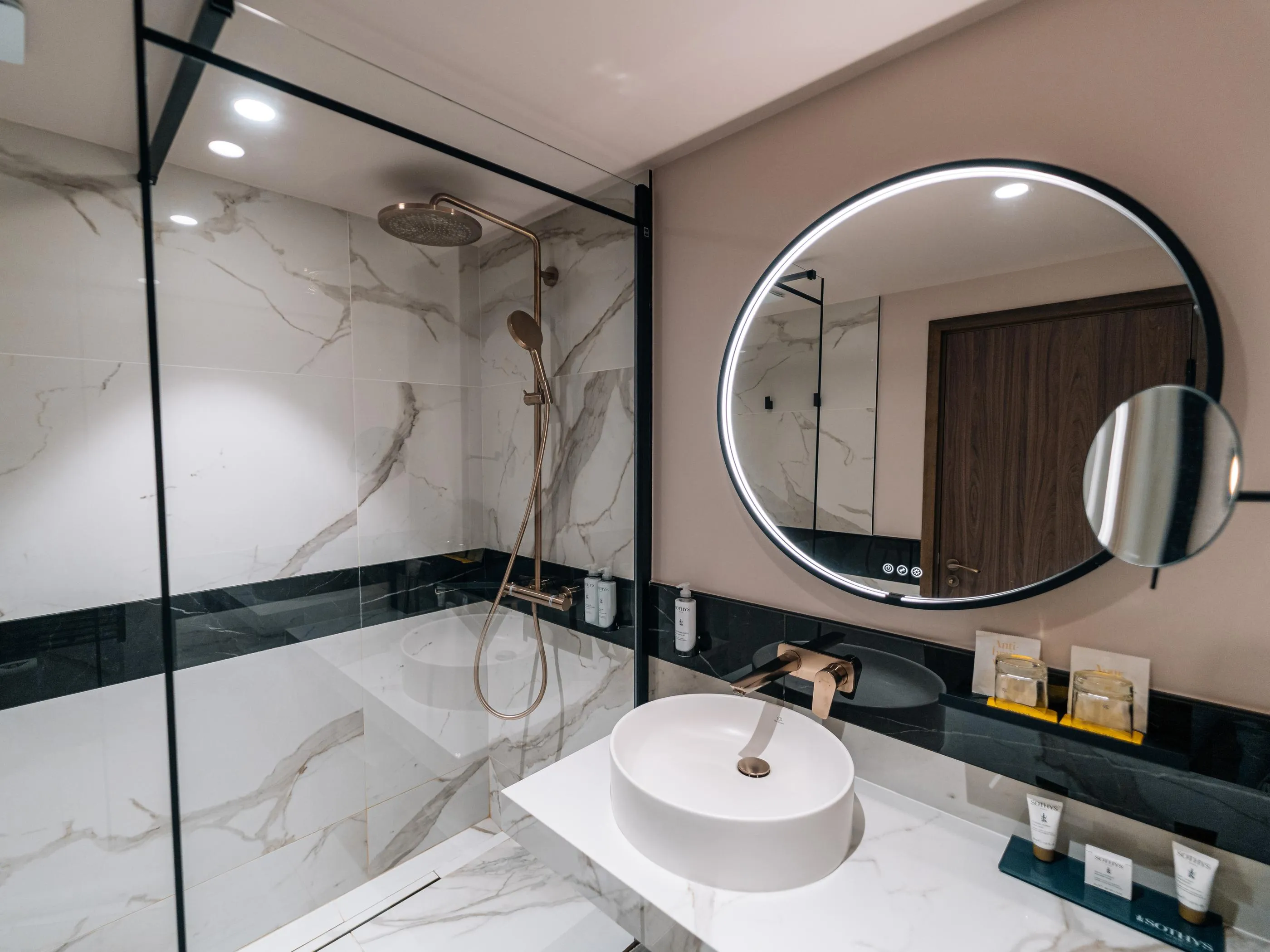 Salle de bain moderne avec douche, lavabo et miroirs circulaires sur fond de marbre blanc et noir