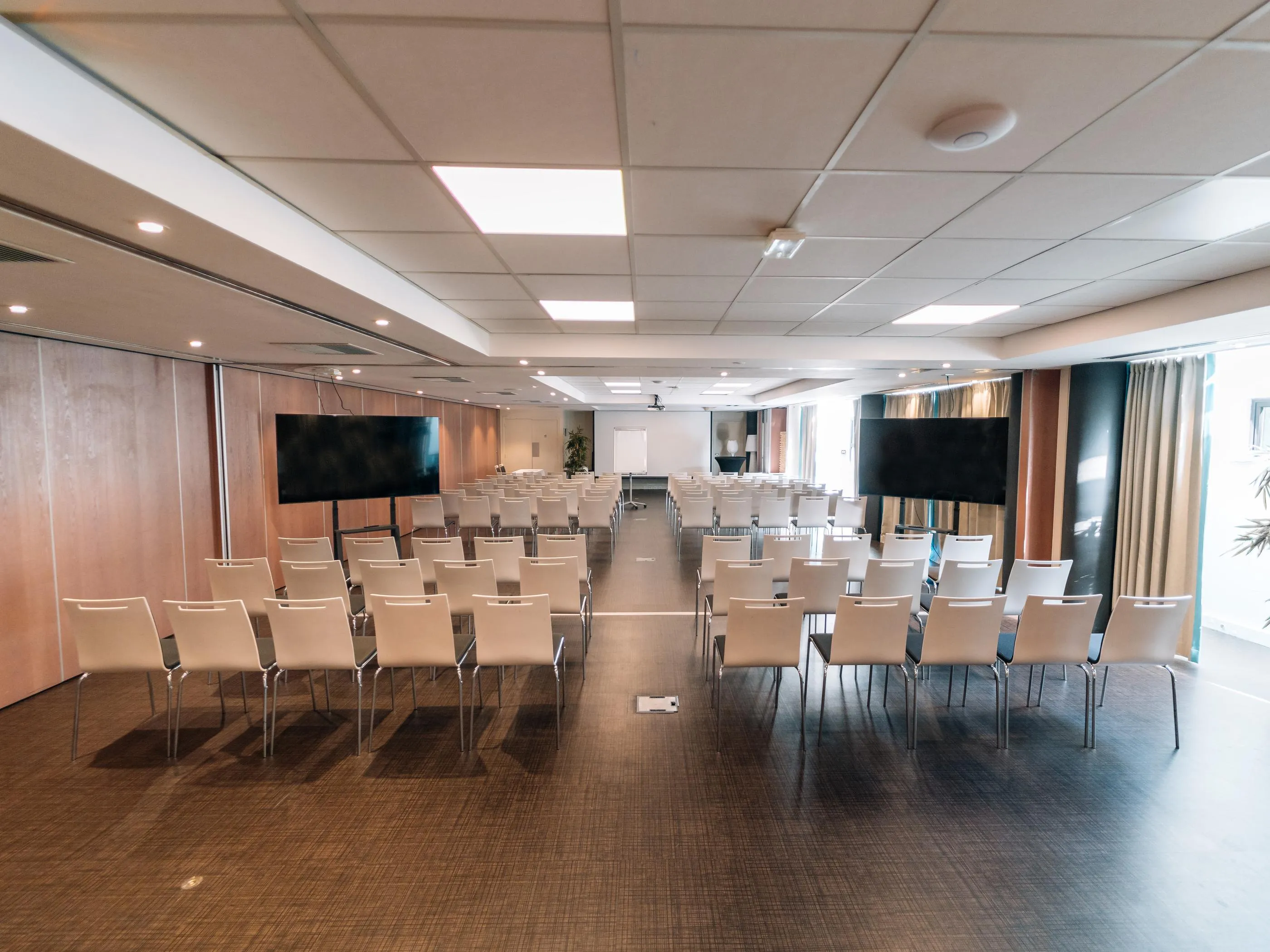 Salle de conférence vide avec des rangées de chaises, deux écrans et des lumières au plafond