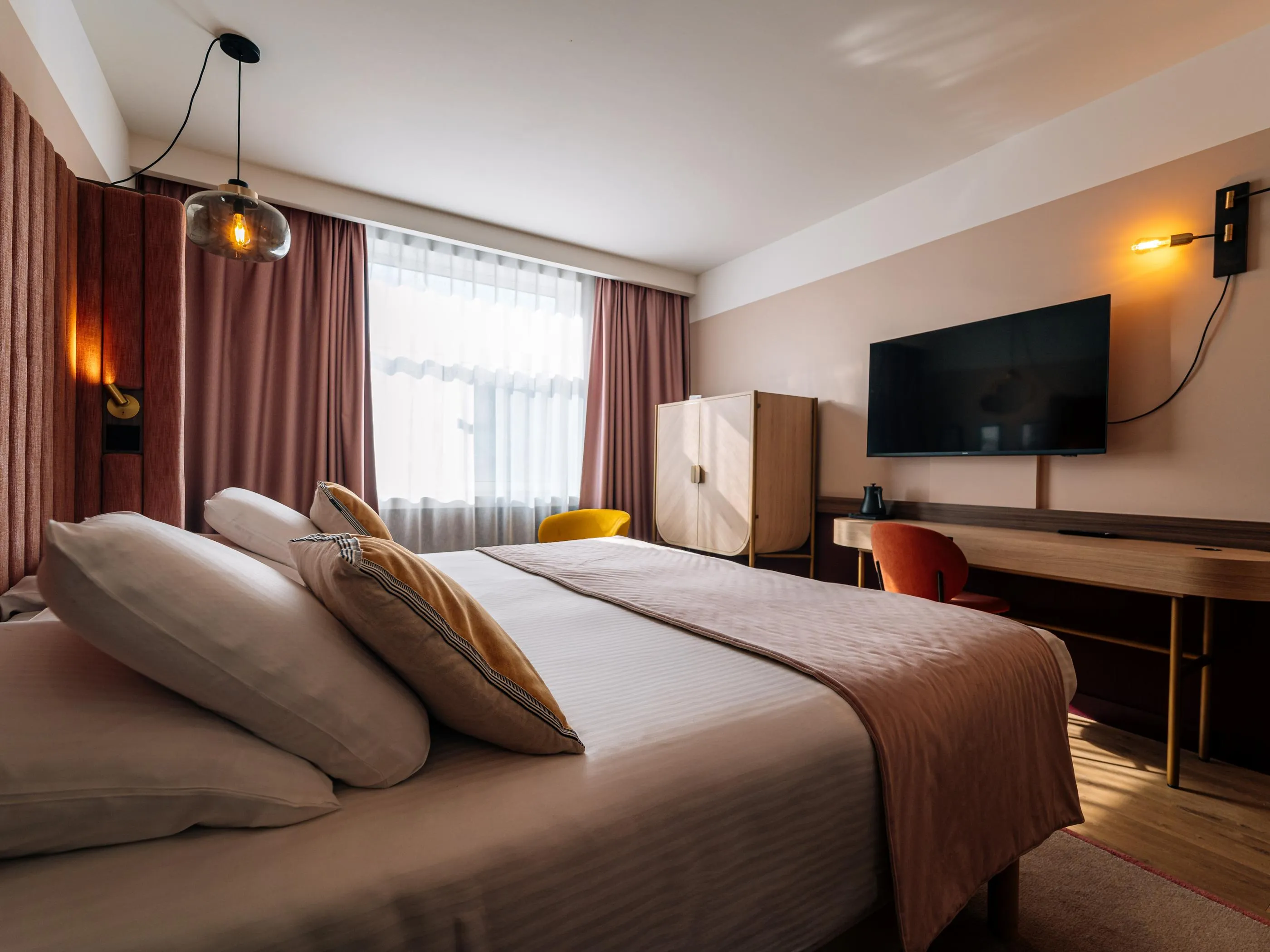 Chambre d'hôtel avec un lit double, une télévision à écran plat, une table de travail et des rideaux marron