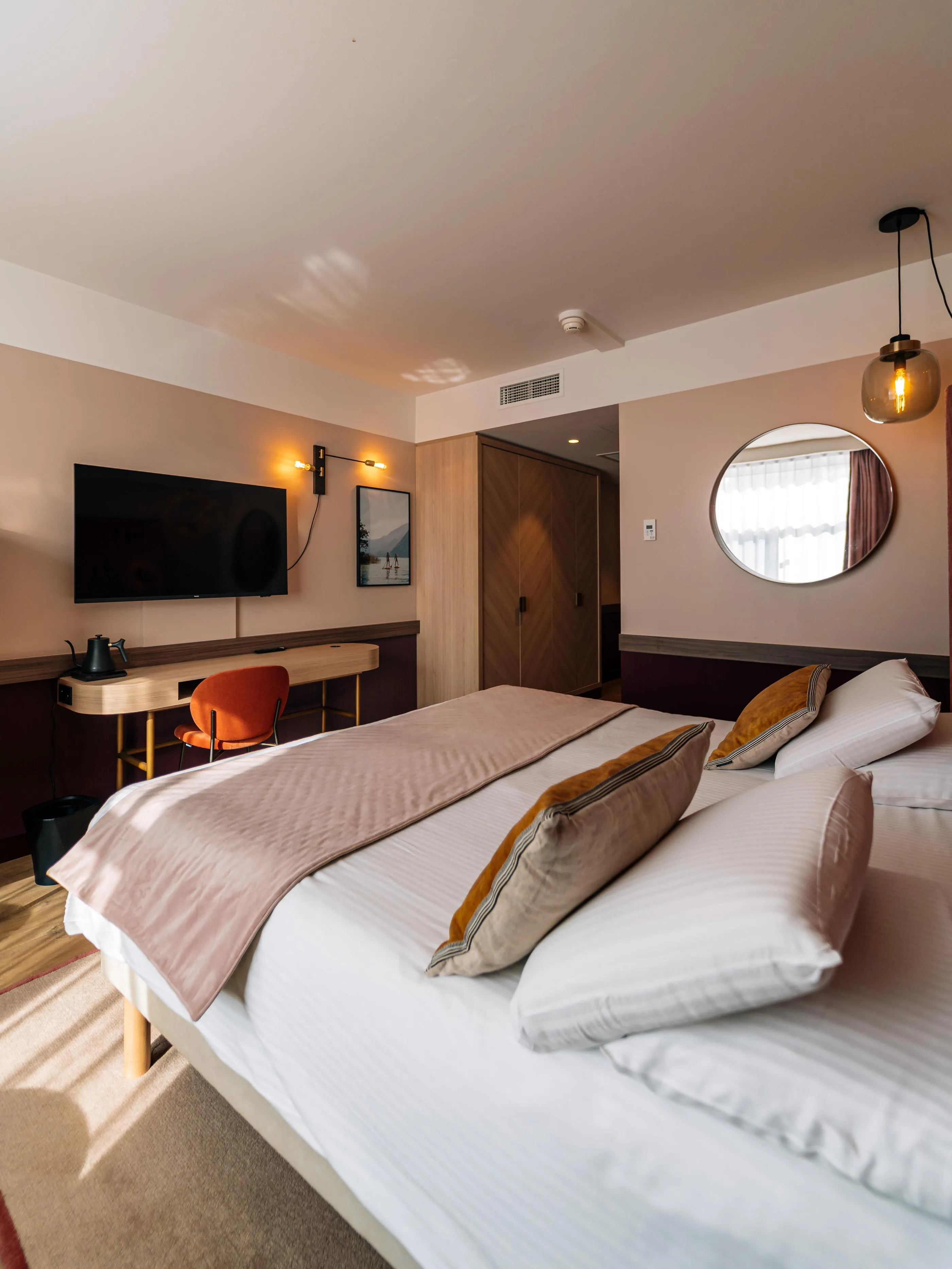 Chambre avec deux lits simples, un bureau, une télévision, un miroir rond et une lampe suspendue