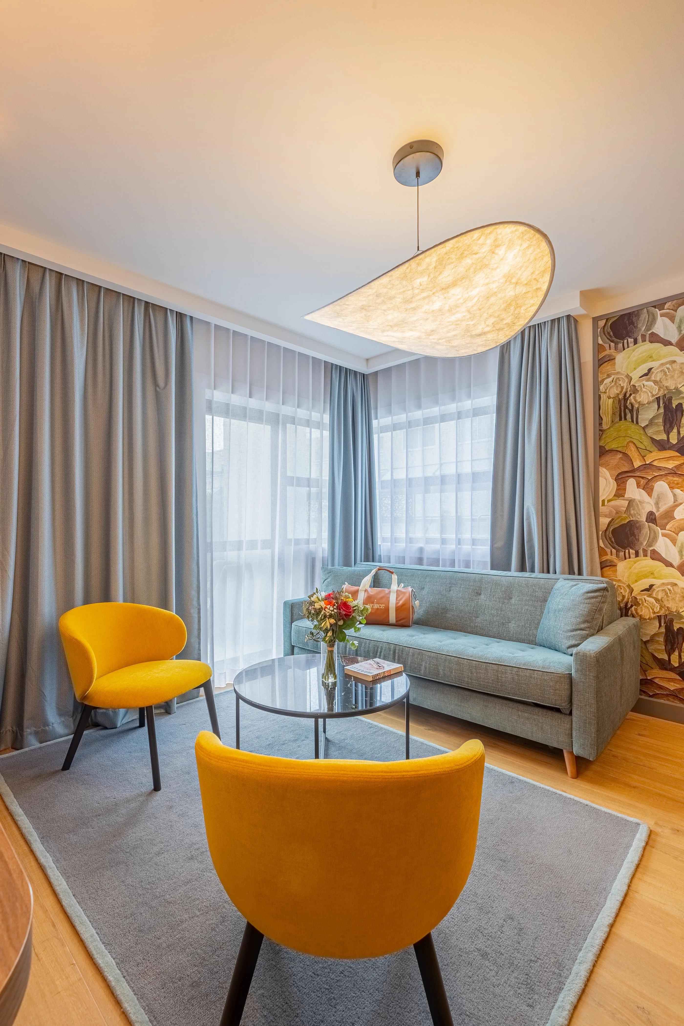 Salon avec canapé gris, deux fauteuils jaunes, table basse, fleurs et lumière suspendue