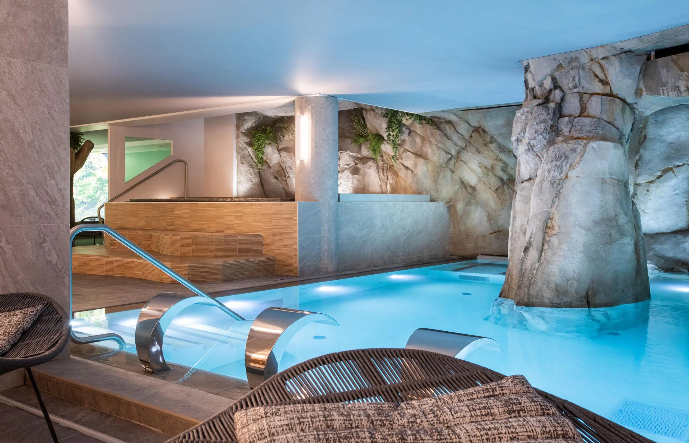 Piscine intérieure avec des rochers décoratifs, des chaises longues en bois et des marches d'accès