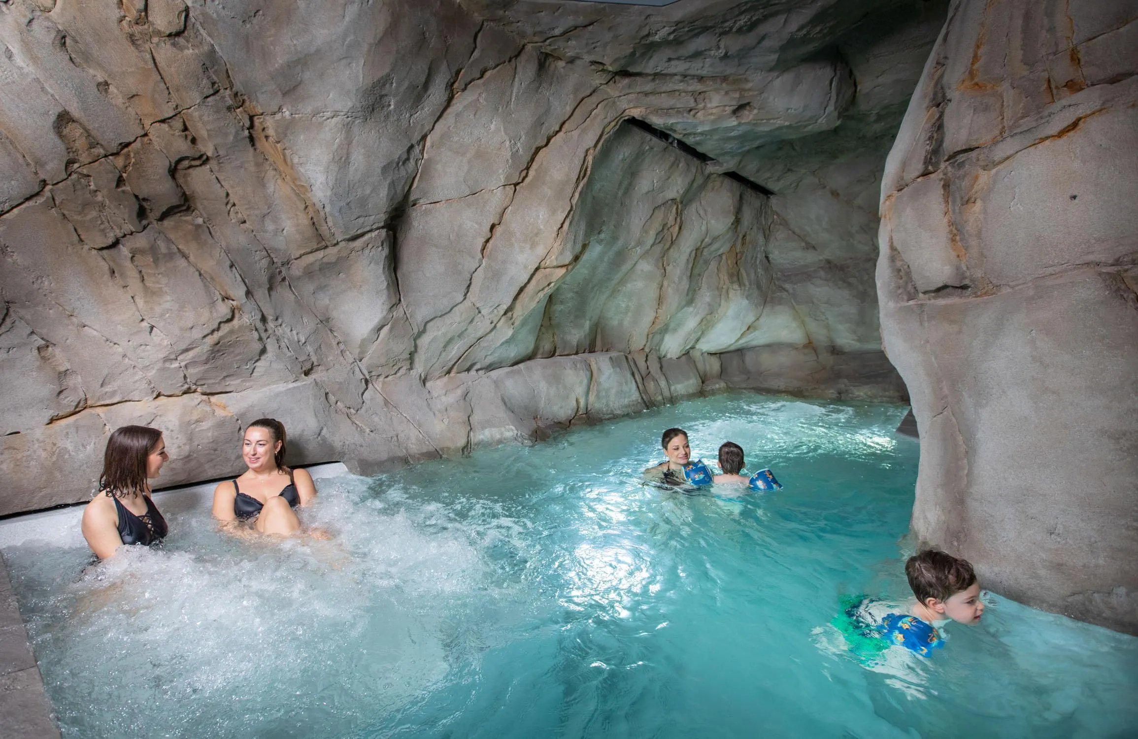 Quatre personnes nagent dans une piscine située dans une grotte rocheuse