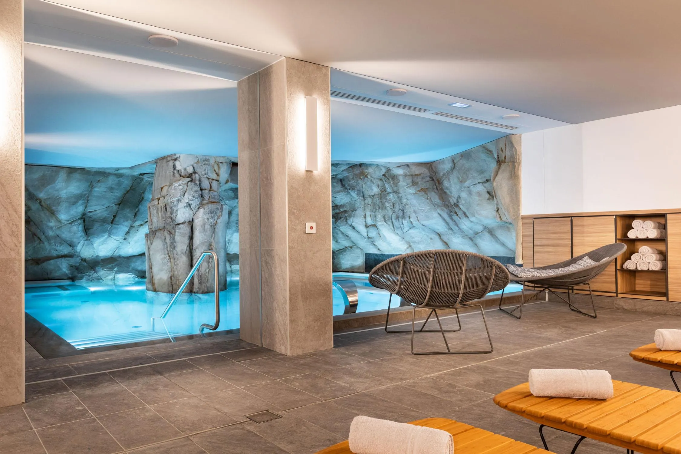 Salle de relaxation avec des chaises longues, des serviettes et une vue sur une piscine avec des rochers peints sur le mur