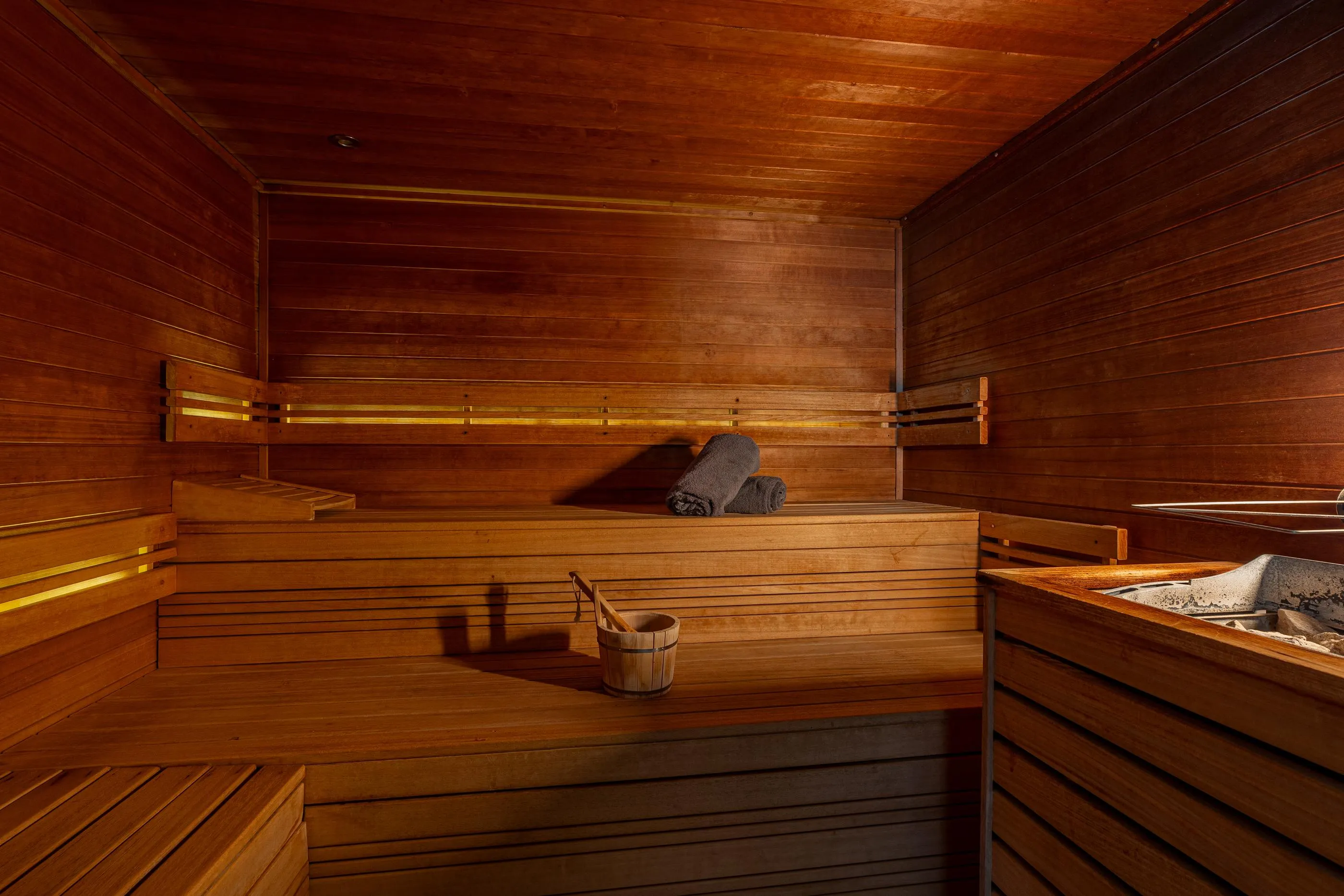 Intérieur d'un sauna en bois avec des bancs, un seau et une louche en bois, et des pierres chaudes