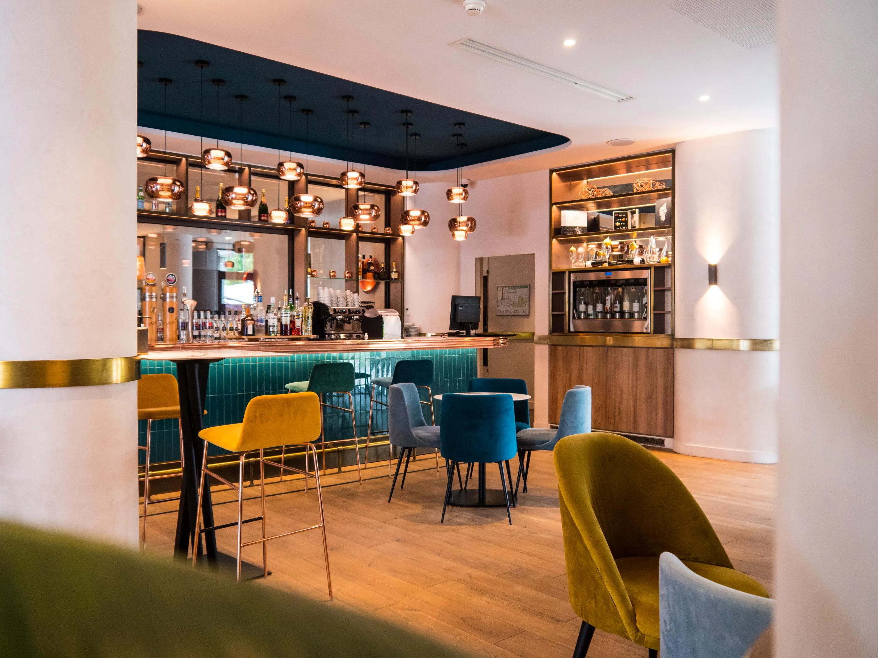 Un bar moderne avec des tabourets colorés, des étagères éclairées et une décoration contemporaine