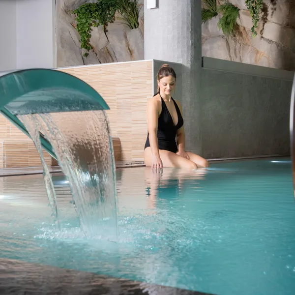 Une femme est assise dans un bassin d'eau avec une cascade artificielle en arrière-plan