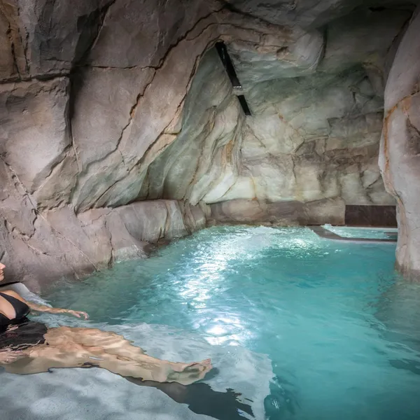 Une personne est allongée dans une piscine d'eau bleue située dans une grotte artificielle en pierre
