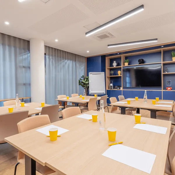 Salle de réunion avec tables, chaises, gobelets, bouteilles d'eau et un écran à l'arrière-plan