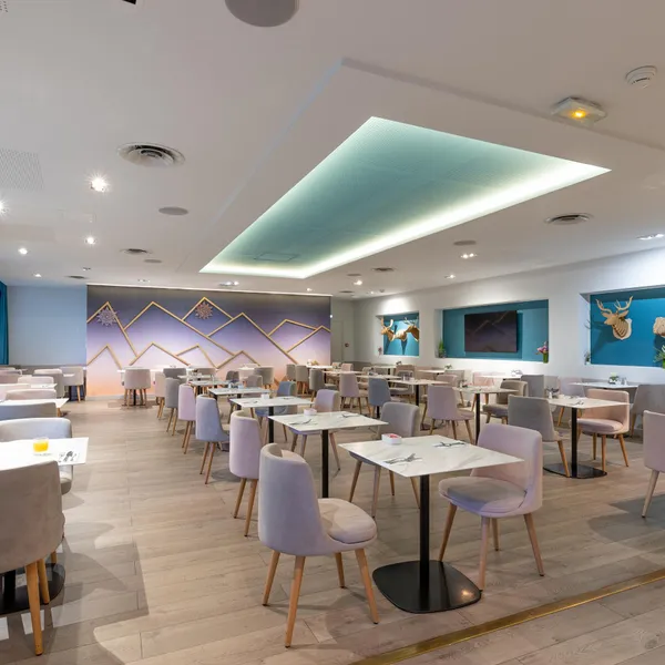 Salle de restaurant moderne avec tables rondes, chaises grises et décor mural aux motifs géométriques et animaux
