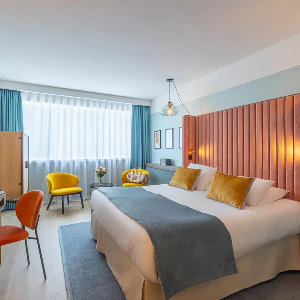 Chambre d'hôtel avec un lit double, un bureau, deux chaises, une table de chevet et des rideaux orange