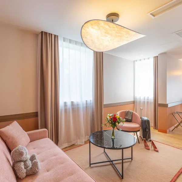 Un salon d'hôtel avec canapé, fauteuil, table basse, luminaire et vue sur une autre pièce