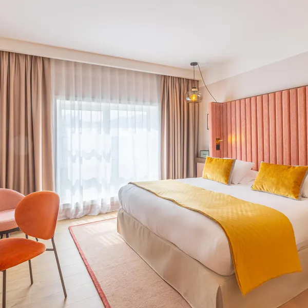 Chambre d'hôtel avec un lit double, des rideaux, une table de travail, deux chaises et une grande fenêtre