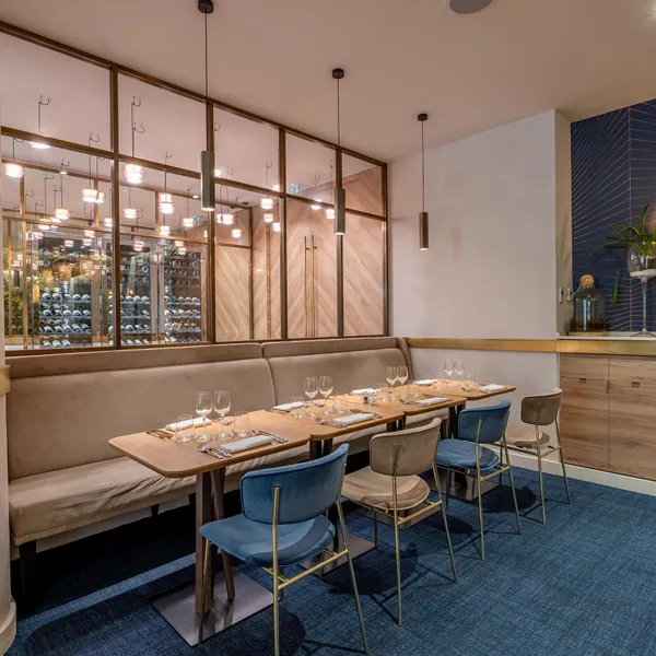 Un restaurant élégant avec une table dressée, des chaises bleues et une banquette, devant une vitrine à vin éclairée