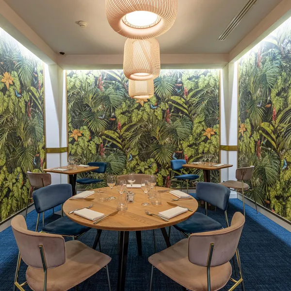 Salle à manger avec des murs couverts d'une végétation luxuriante et des tables rondes entourées de chaises rembourrées
