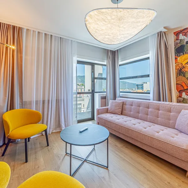 Salon moderne avec canapé beige, deux fauteuils jaunes, table basse, télévision et grande fenêtre avec vue sur la ville