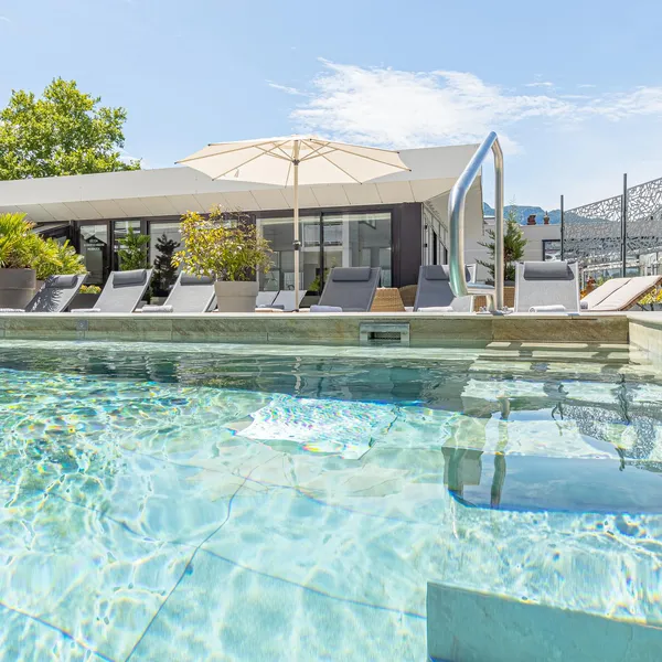 Piscine avec une vue sur une terrasse aménagée de chaises longues, de parasols et de végétation