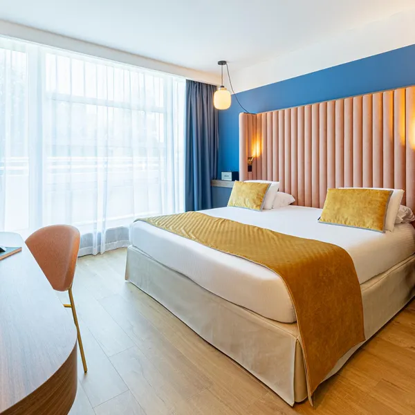 Chambre d'hôtel avec un lit double, une table de travail, des fenêtres avec des rideaux et des lumières murales