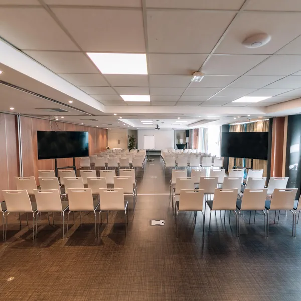 Salle de conférence vide avec des rangées de chaises, deux écrans et des lumières au plafond