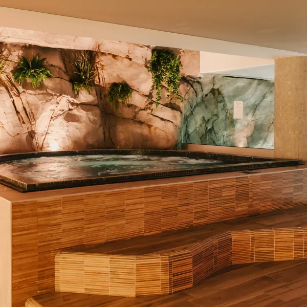 Piscine intérieure avec paroi rocheuse décorée de plantes vertes et bancs en bambou à proximité