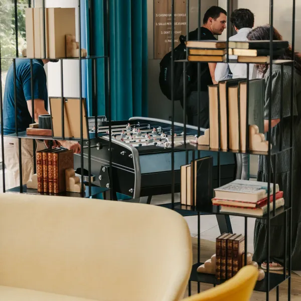 Des personnes jouent à un baby-foot dans un espace intérieur avec des étagères remplies de livres et des canapés